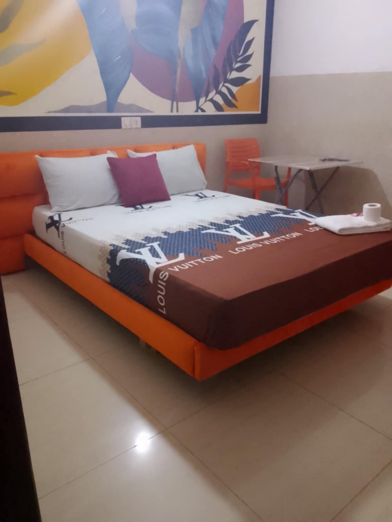 Una cama con una manta Louis Vuitton, cabecera naranja y almohadillas.