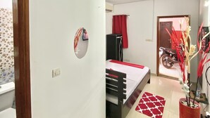 Un dormitorio con cama, espejo, alfombra roja y una planta en maceta.