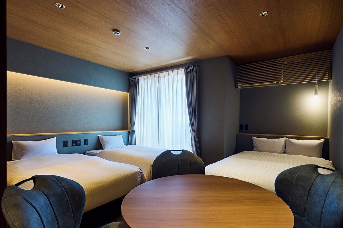 Habitación de hotel con dos camas, una mesa redonda e iluminación empotrada en el techo.