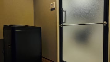 Ein kleines Zimmer mit einem Kühlschrank, einer Tür mit Milchglasfenster und einem an der Wand montierten Thermostat.