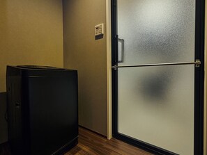 Una habitación compacta con refrigerador, una puerta con panel de vidrio esmerilado y un termostato montado en la pared.