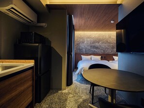 Una habitación de hotel compacta con kitchenette, una cama con ropa blanca y una pequeña mesa de comedor.