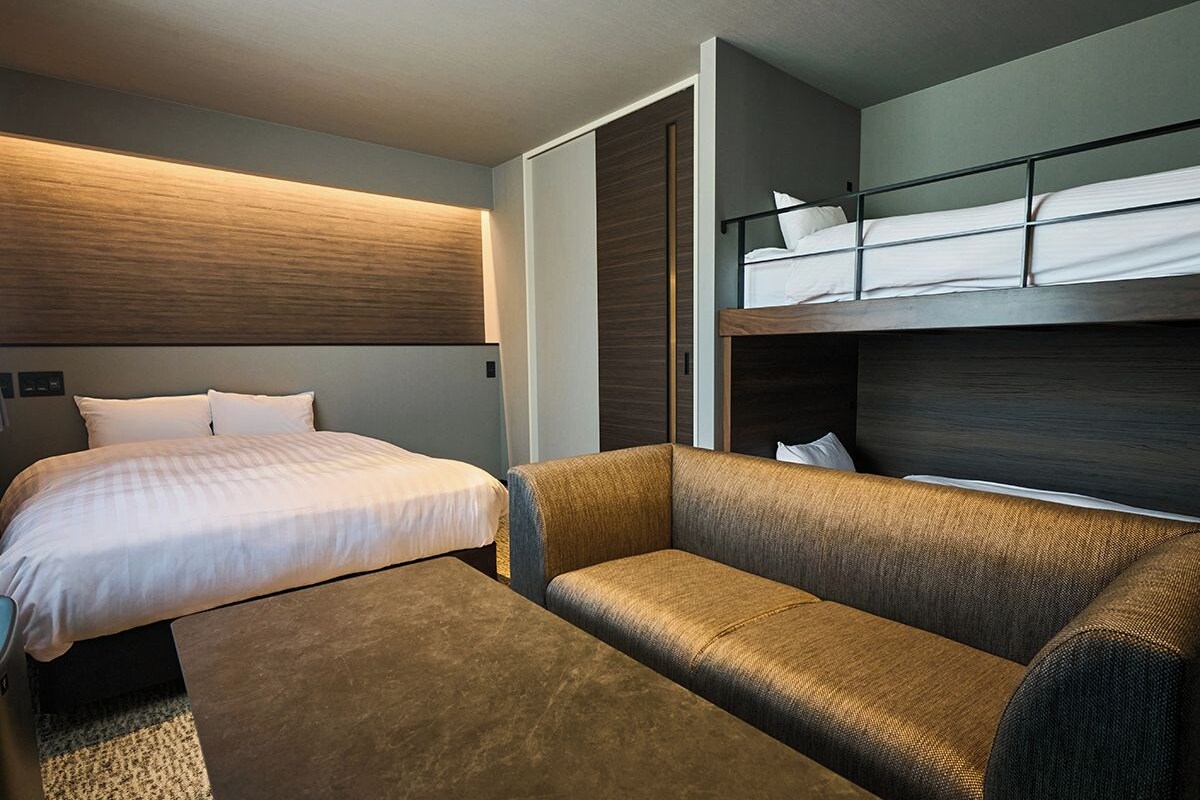 Una habitación de hotel moderna con cama, sofá y literas.