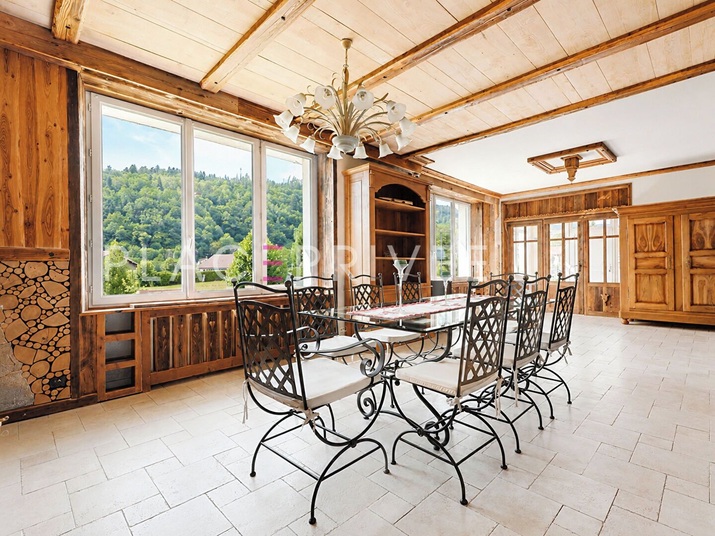 Un espace repas avec une grande table et des chaises, des murs en bois et une vue sur la verdure grâce à de grandes fenêtres.