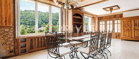 Un espace repas avec une grande table et des chaises, des murs en bois et une vue sur la verdure grâce à de grandes fenêtres.