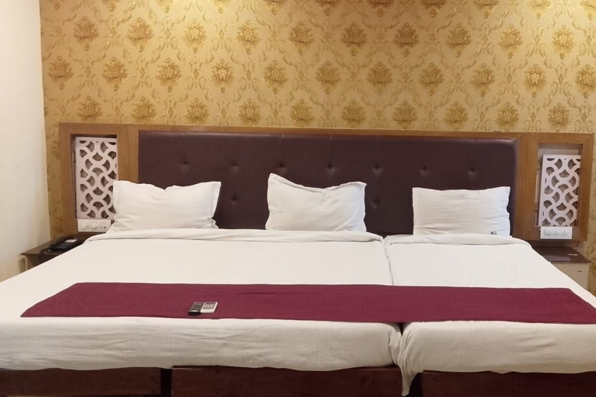 Quarto de hotel com uma cama grande, duas mesas de cabeceira, um painel de cabeceira em madeira, papel de parede estampado e uma janela com design geométrico.