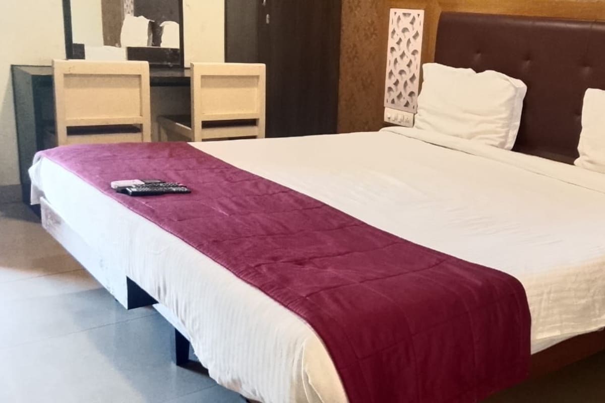 Cama com colcha branca e bordô, mesa de cabeceira com telefone e cabeceira com padrão decorativo.