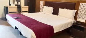 Cama com colcha branca e bordô, mesa de cabeceira com telefone e cabeceira com padrão decorativo.