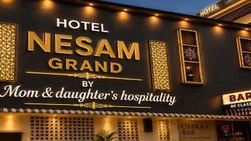 Um hotel chamado 'Nesam Grand' com uma placa indicando 'Hospitalidade de mãe e filha'.