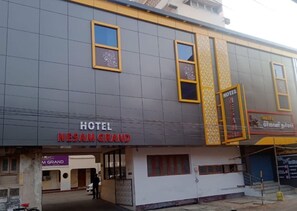 A hotel named 'Nesam Grand' with a modern facade, large windows, and a visible entrance.