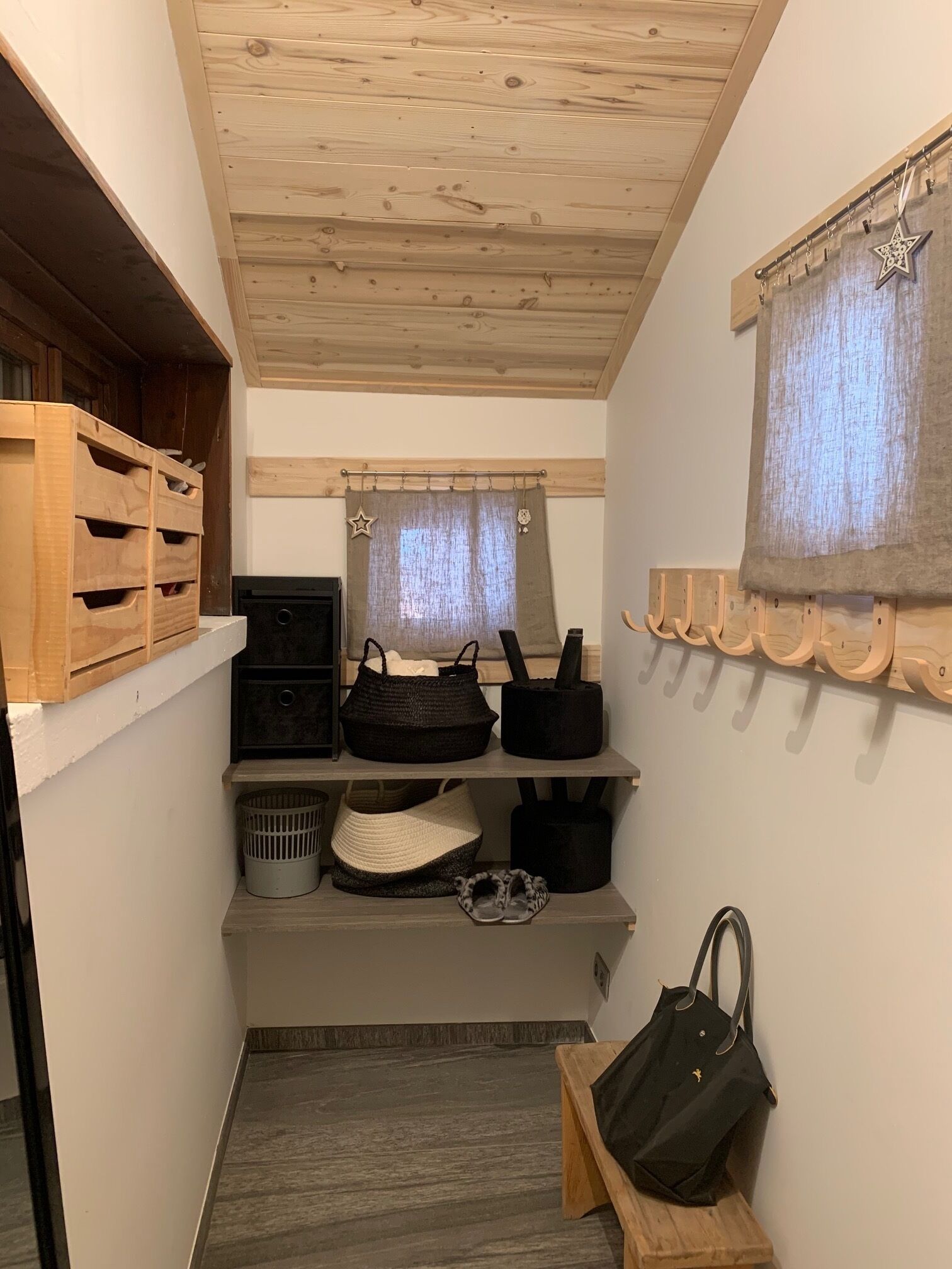 Un couloir étroit avec des étagères en bois, un banc et un porte-manteau suspendu.