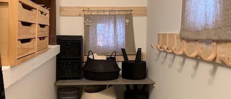A narrow hallway with wooden shelves, a bench, and a hanging coat rack.