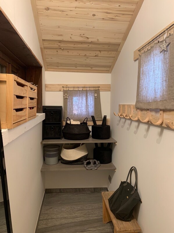 A narrow hallway with wooden shelves, a bench, and a hanging coat rack.