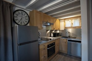 Eine kompakte Küche mit Holzschränken, einem Edelstahlkühlschrank, einer Mikrowelle, einem Wasserkocher und einem Geschirrspüler.