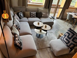 A modern living room with a sectional sofa, two round coffee tables, and a view of the outdoors.