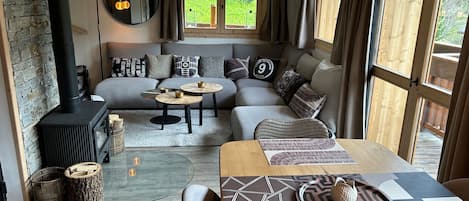 A cozy living room with a fireplace, a sofa set, a dining table, and a large window with curtains.