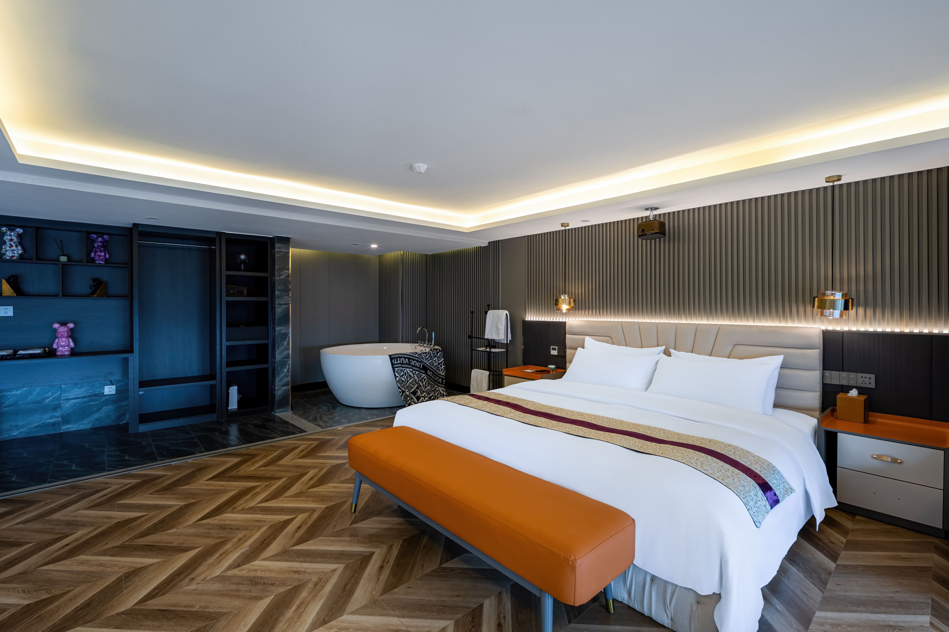 A modern hotel room with a large bed, a bench, a bathtub, and a vanity with shelves.