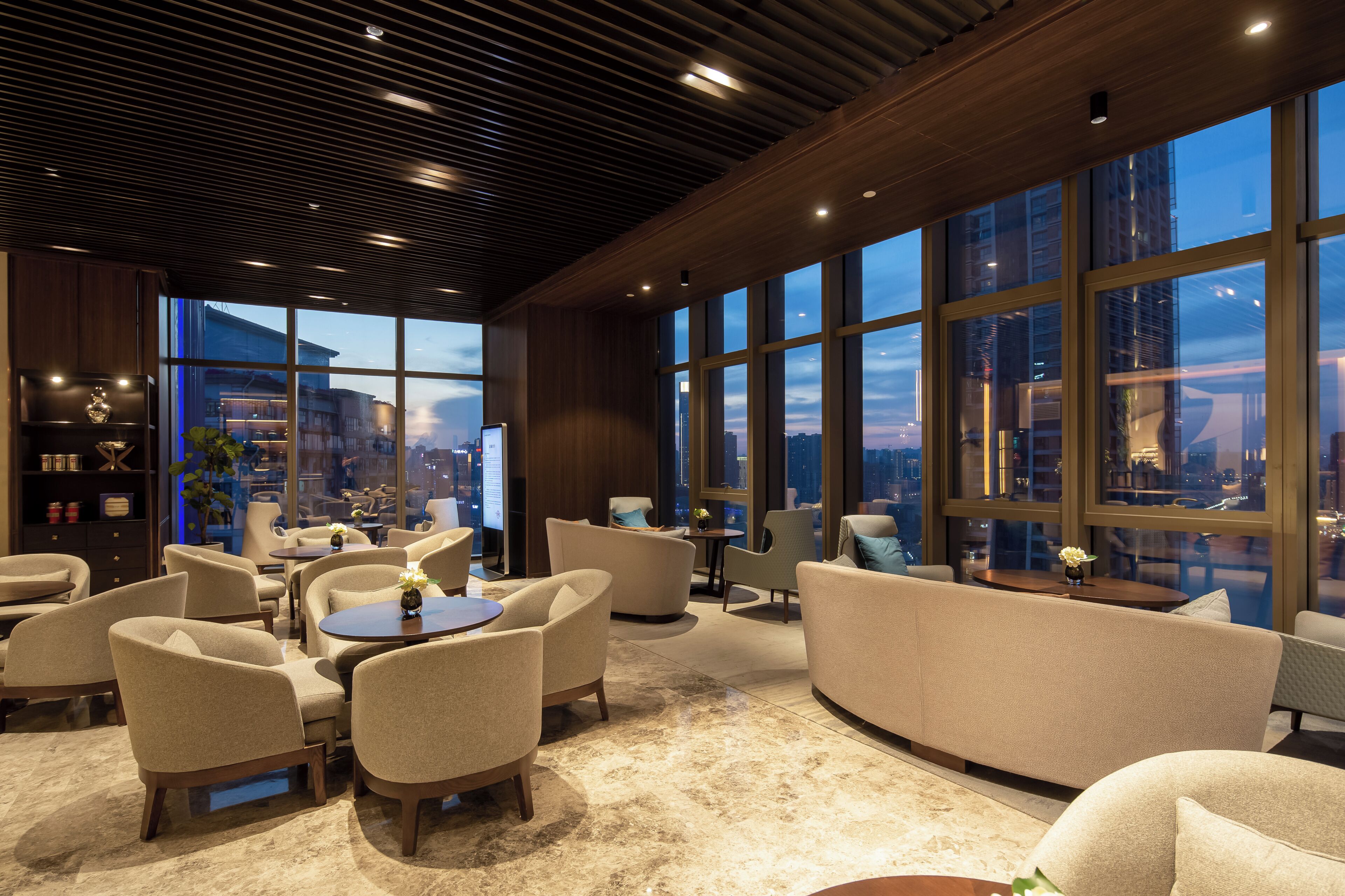 A modern lounge area with seating, a coffee table, and a view of the cityscape through large windows.