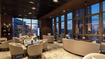 A modern lounge area with seating, a coffee table, and a view of the cityscape through large windows.