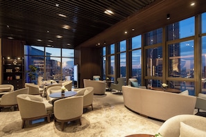 A modern lounge area with seating, a coffee table, and a view of the cityscape through large windows. - Chongqing Ashan River View Hotel (Chongqing)