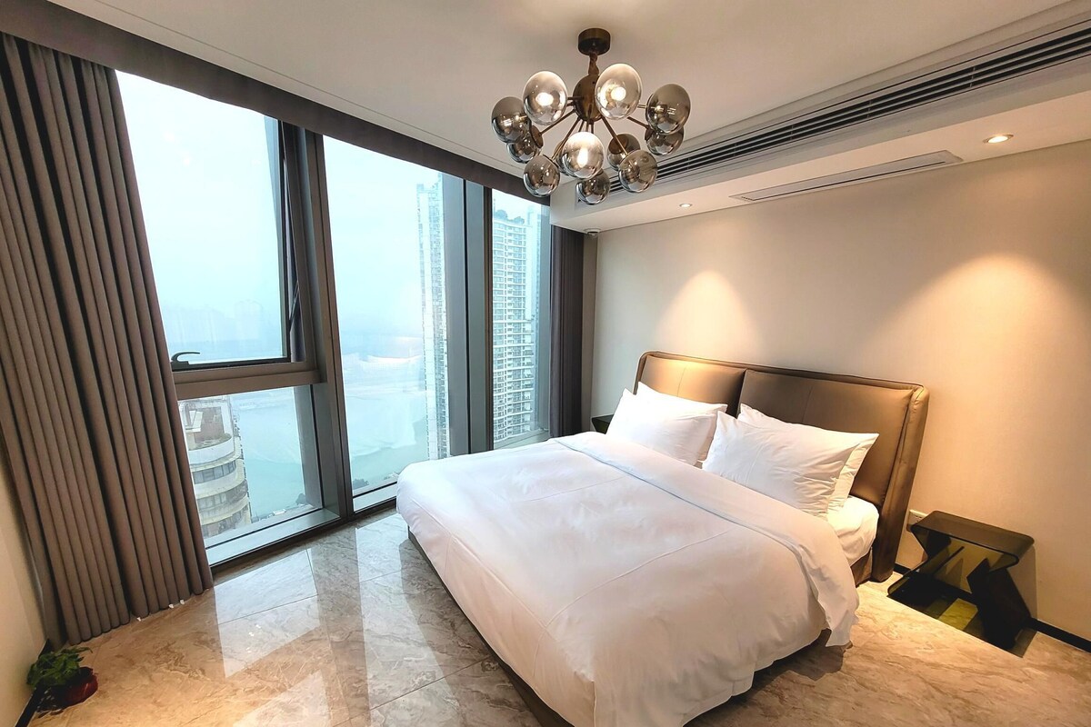 A hotel room with a large bed, a chandelier, a view of the city, and a modern design.