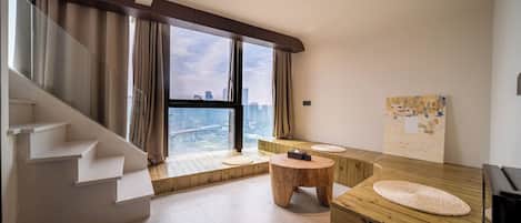 A modern interior with a staircase, a wooden bench, a round wooden table, and a large window with a city view.
