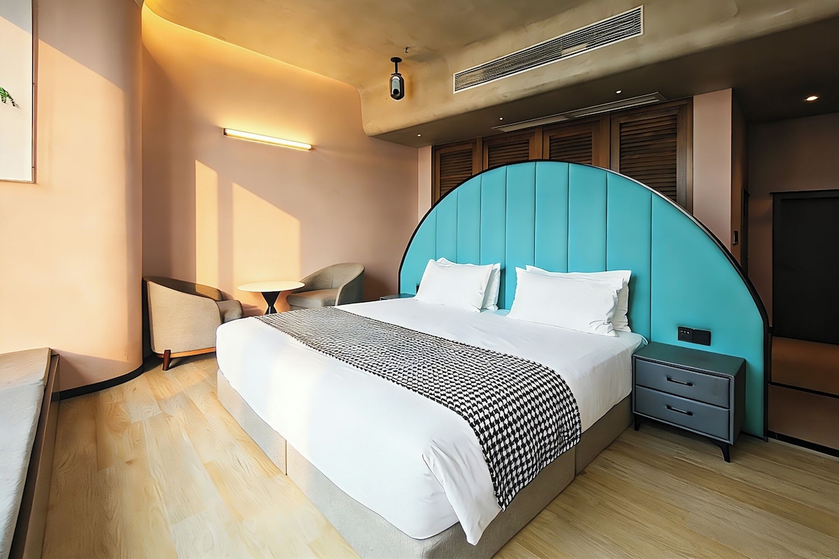 A modern hotel room with a large bed, bedside tables, a desk, and a chair.