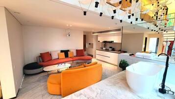 Una sala de estar moderna con sofá, reposapiés y una zona de cocina con lavamanos y armarios.