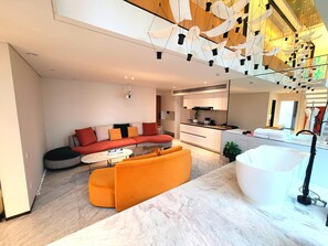 Una sala de estar moderna con sofá, reposapiés y una zona de cocina con lavamanos y armarios.