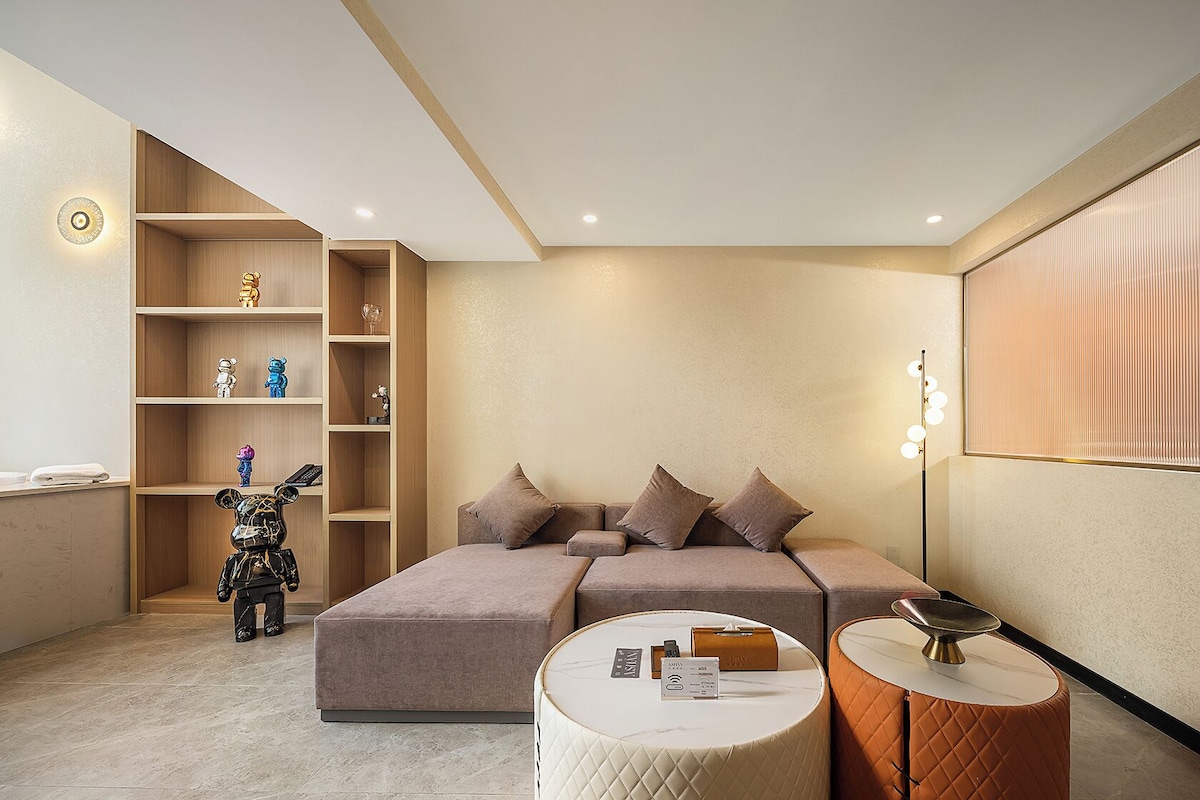 A modern bedroom with a sofa bed, a small round table, a bookshelf, and a lamp.