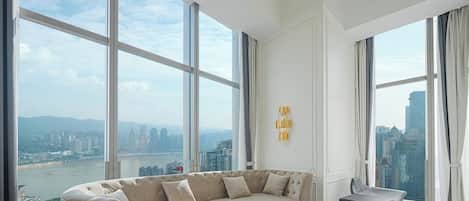 Una sala de estar moderna con un sofá grande, una mesa de centro y vistas a un paisaje urbano a través de amplios ventanales.