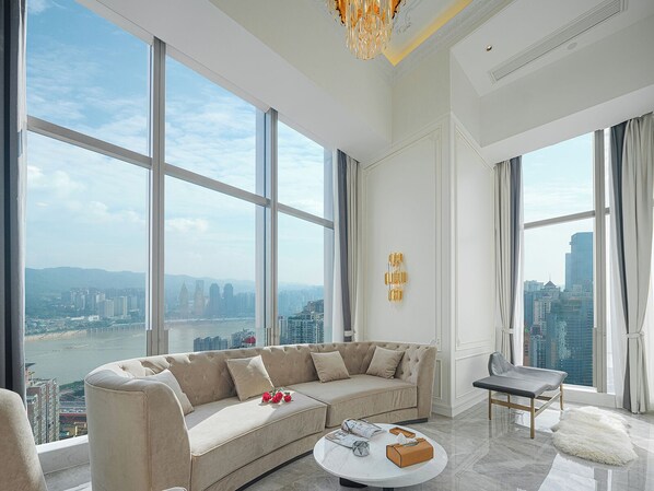 Una sala de estar moderna con un sofá grande, una mesa de centro y vistas a un paisaje urbano a través de amplios ventanales.