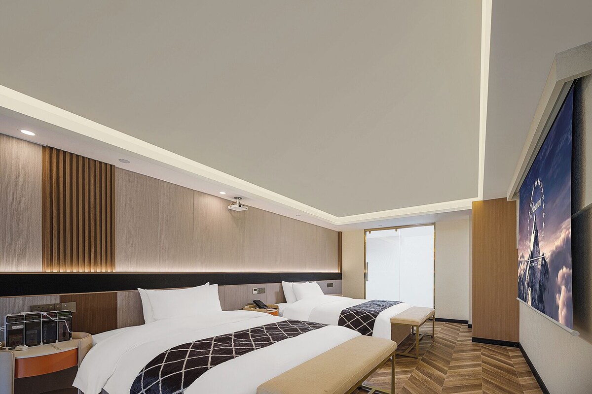 A modern hotel room with a large bed, bedside tables, and a large window.