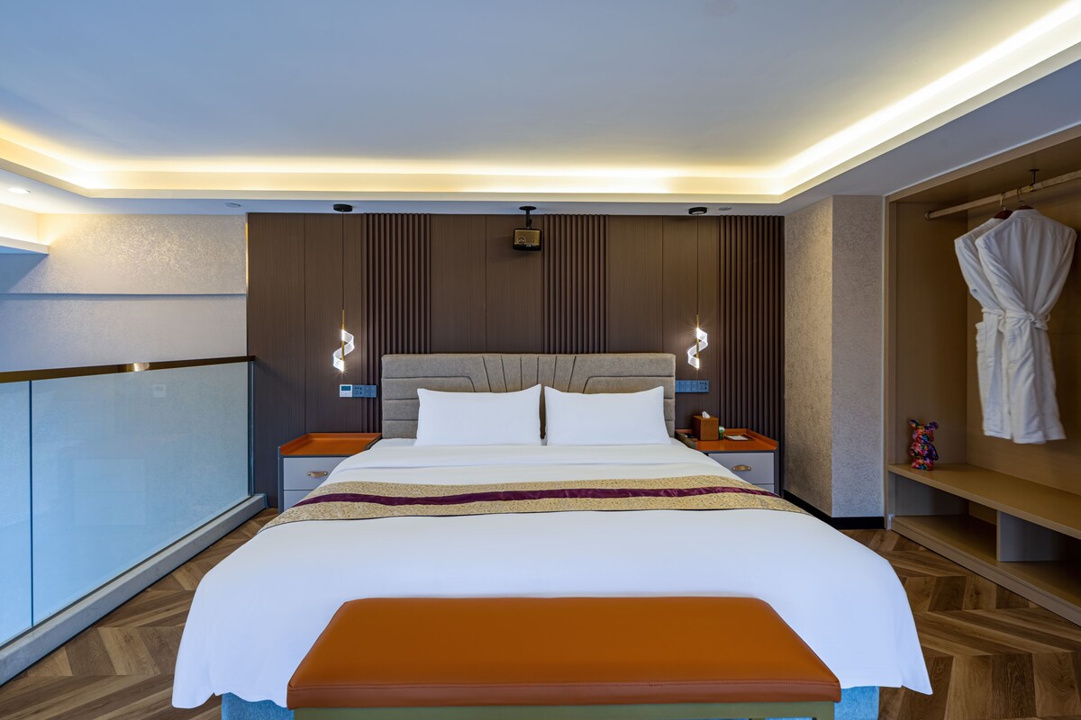 A hotel room with a large bed, bedside tables, a robe rack, and a bench.