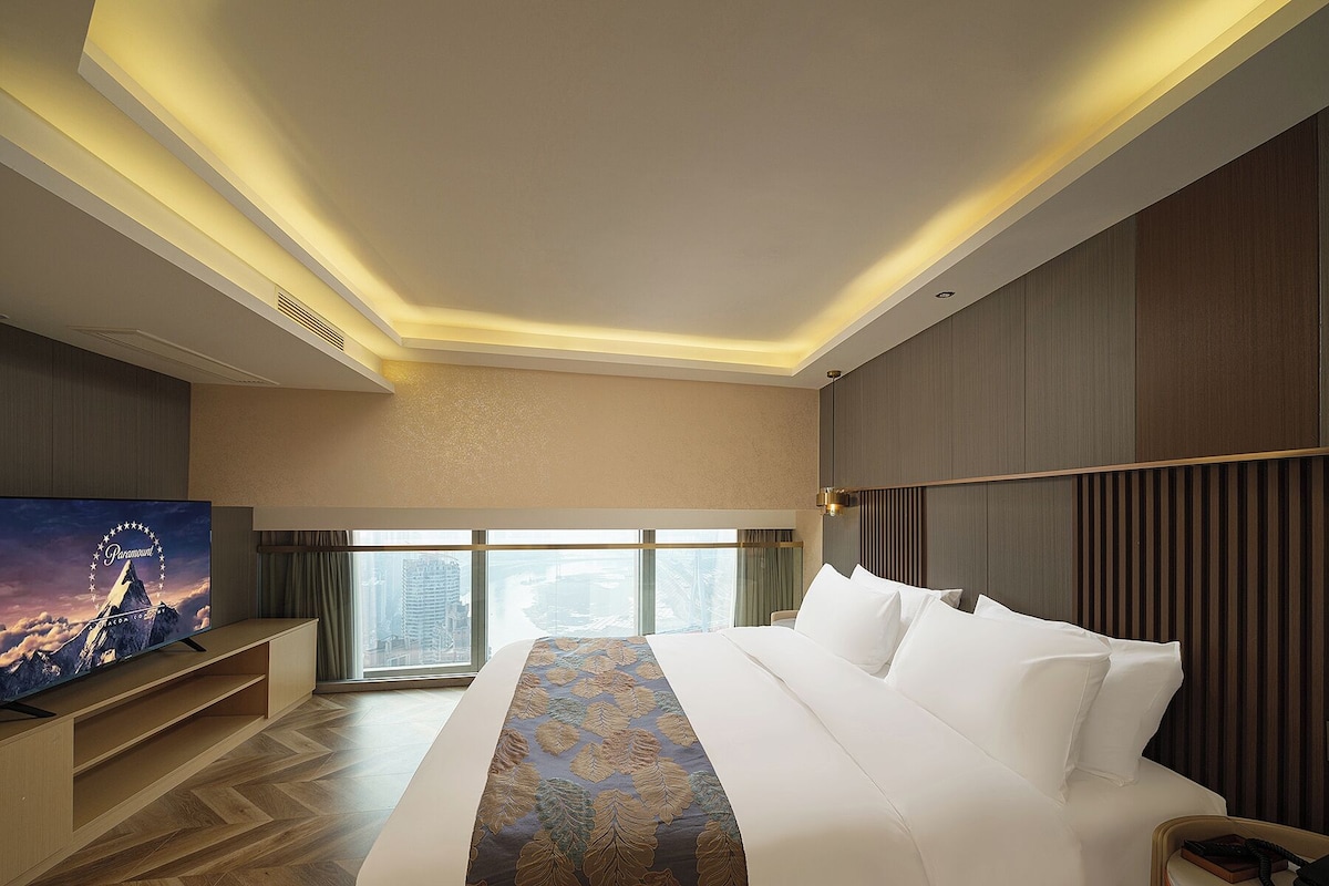 A hotel room with a large bed, a television, and a view of the cityscape.