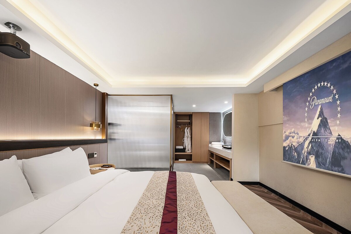 A hotel room with a large bed, a walk-in closet, a bathroom with a vanity, and a wall-mounted television.