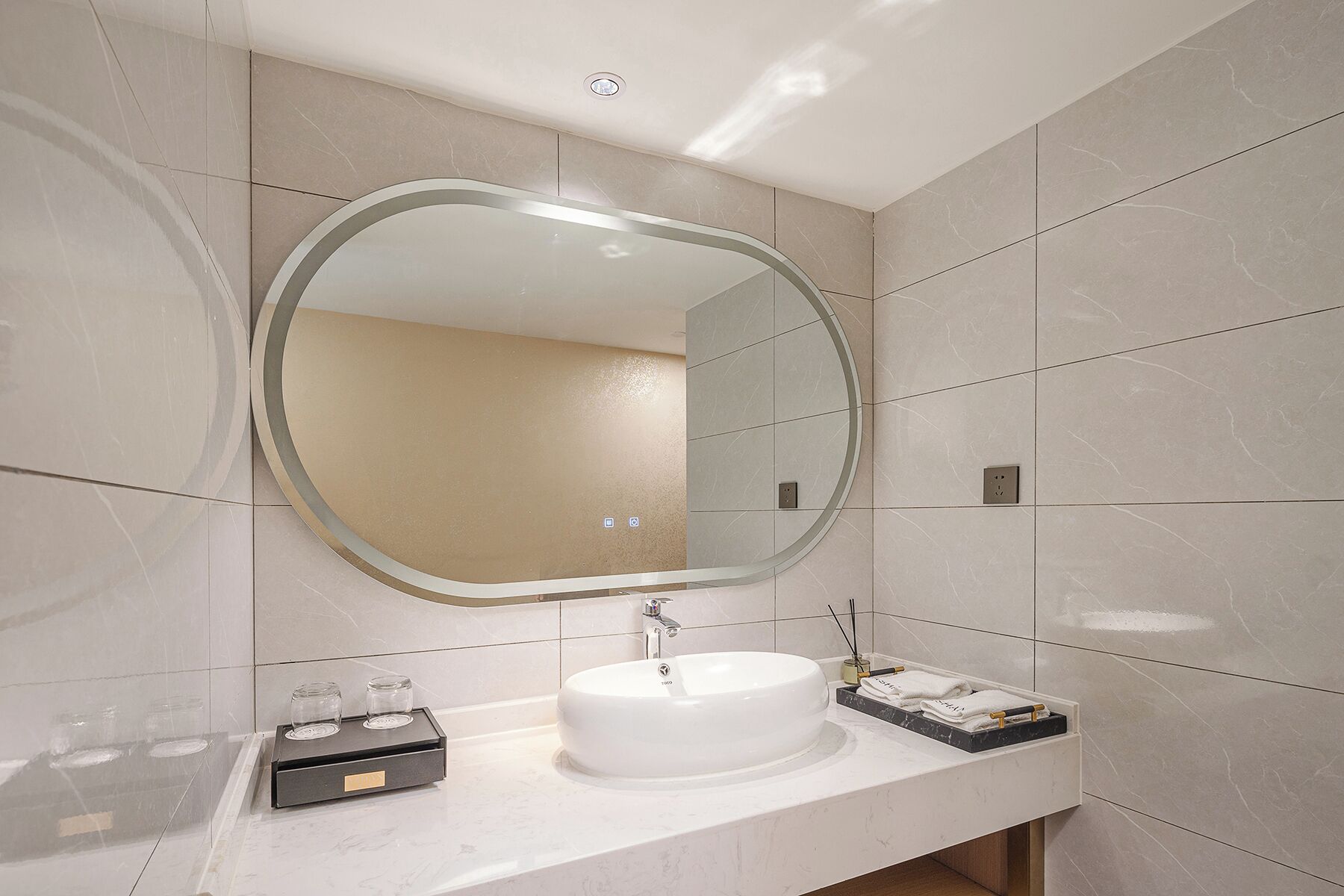 Un baño moderno con un espejo redondo, un lavabo blanco y un pequeño estante con artículos de aseo.