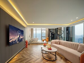 A modern living room with a large flat-screen TV, a sofa, a coffee table, and a view of a cityscape through large windows. - Chongqing Ashan River View Hotel (Chongqing)