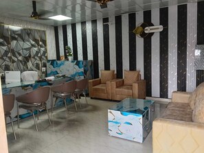 A modern living room with a sofa, chairs, a glass coffee table, and a dining area with a table and chairs. - Mansa Hotel and Lawn (Lucknow)