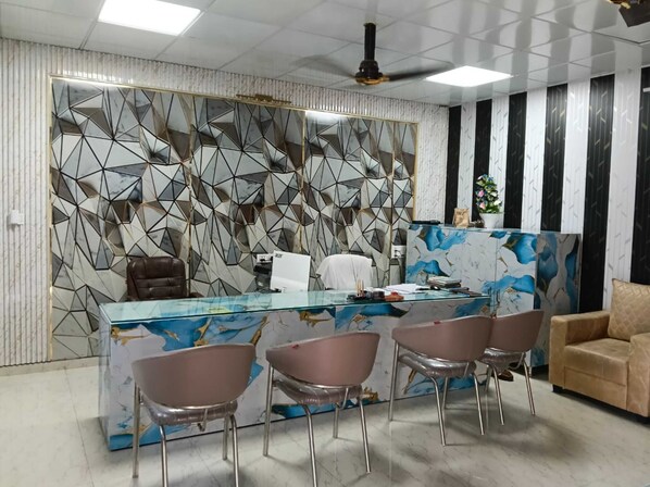 Un área de recepción con pared de diseño de mármol, mostrador de vidrio y sillas modernas.