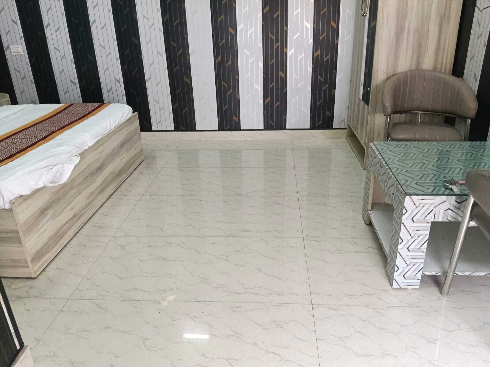A room with a bed, a table, and a chair. The floor is tiled.