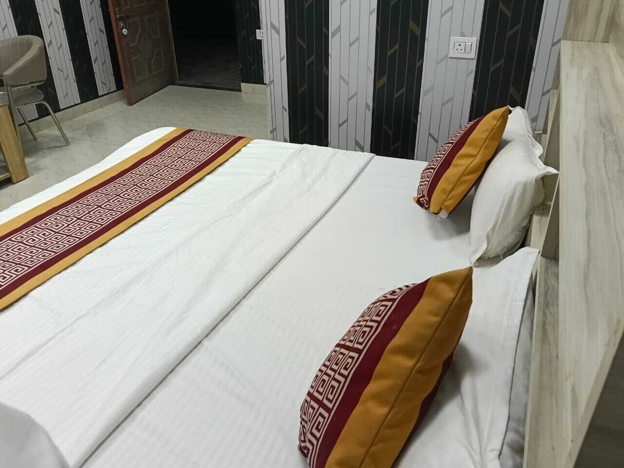 Una cama con colcha estampada y dos almohadas, una silla y una puerta en una habitación con paredes decoradas.