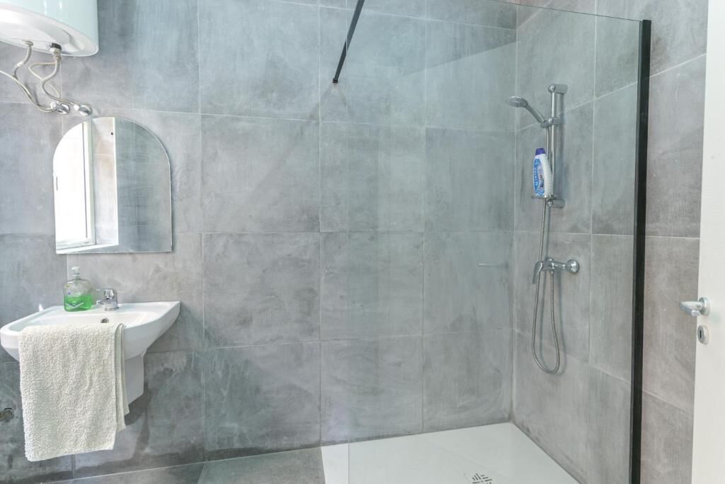A modern bathroom with a glass shower enclosure, a sink with a mirror, and a towel hanging on the wall.
