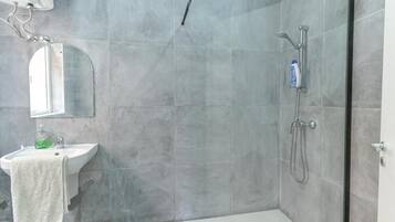 A modern bathroom with a glass shower enclosure, a sink with a mirror, and a towel hanging on the wall.
