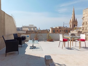 Eine Dachterrasse mit Gartenmöbeln, Blumentöpfen und Blick auf eine Stadtlandschaft, darunter ein Kirchturm.