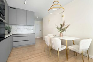 A modern kitchen with grey cabinets, a marble countertop, and a dining area with a white table and chairs. - Spacious Apartment with a balcony | Close to the Airport (Poznań)