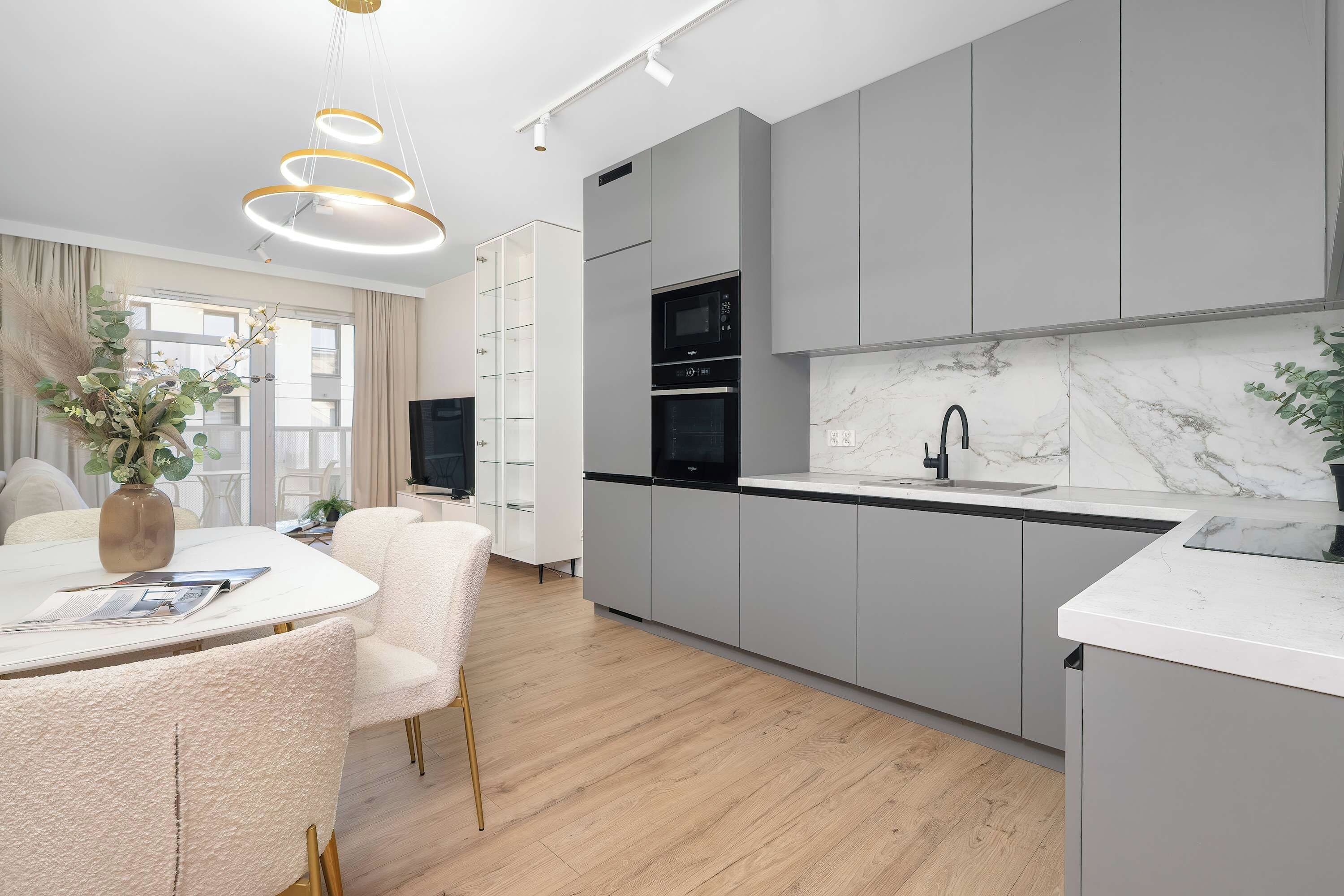 Une cuisine moderne avec des meubles gris, un plan de travail en marbre et un four encastré.