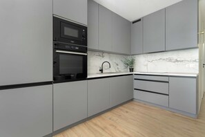 Een moderne keuken met grijze kastjes, een zwarte magnetron en een dubbele oven.