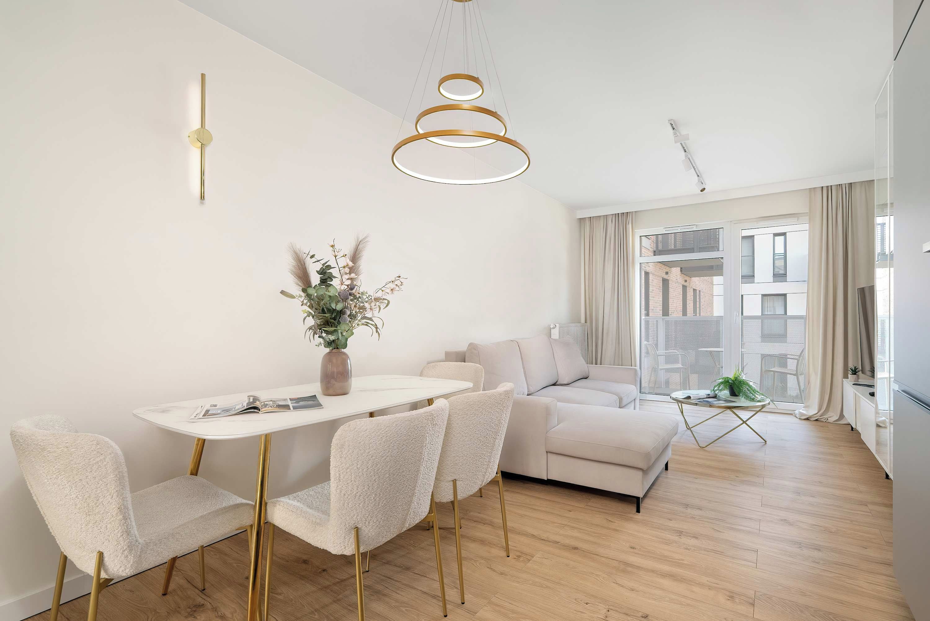 A modern living room with a dining area, featuring a white sofa, a round coffee table, and a dining table with chairs.