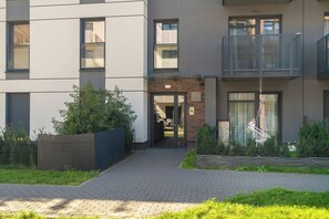 A modern apartment building with a brick entrance, a small garden area, and a metal balcony. - Spacious Apartment with a balcony | Close to the Airport (Poznań)